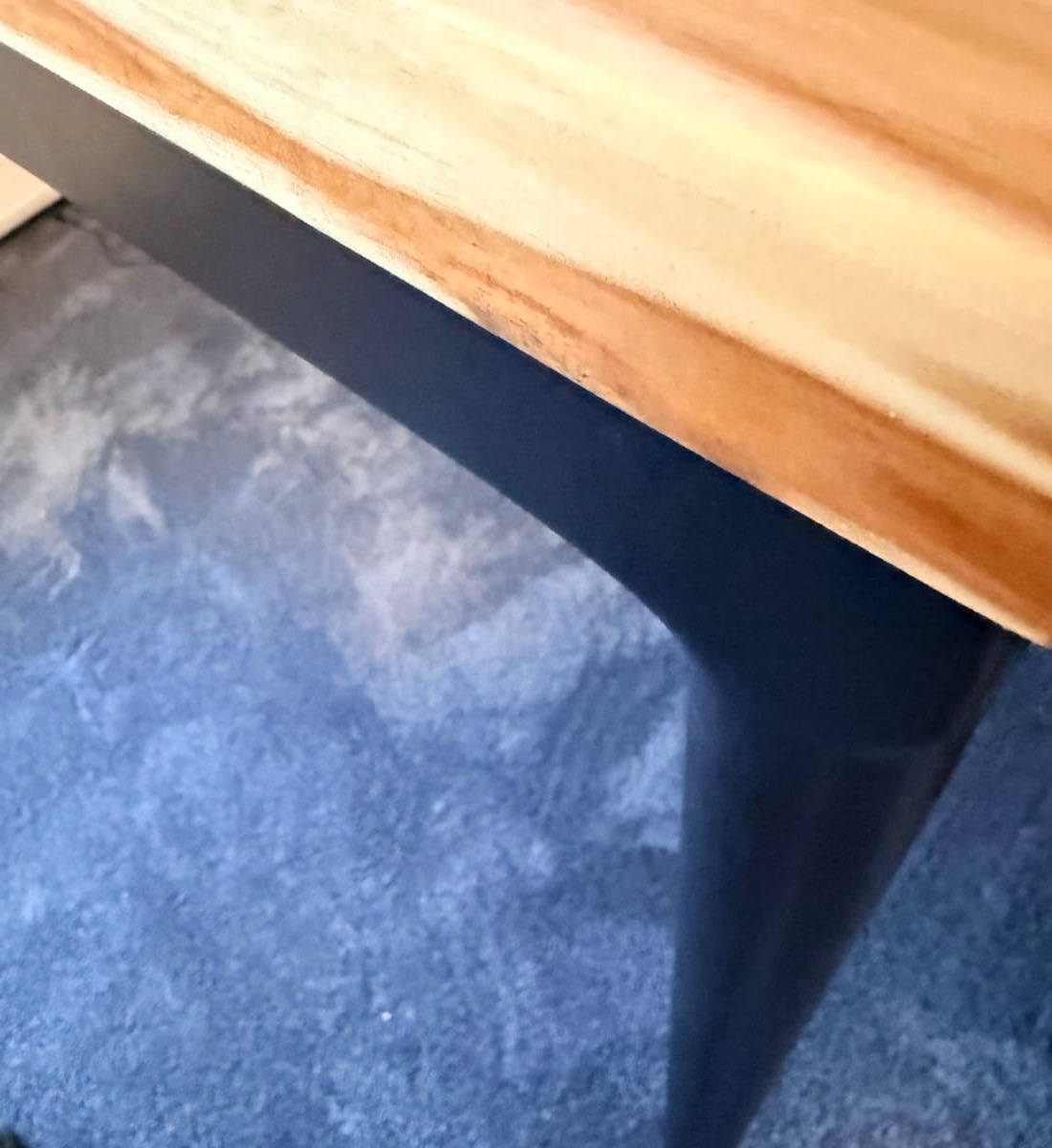 Single tapered Parsons leg at floor level showing the slim profile and matte black finish meeting the dark blue carpet