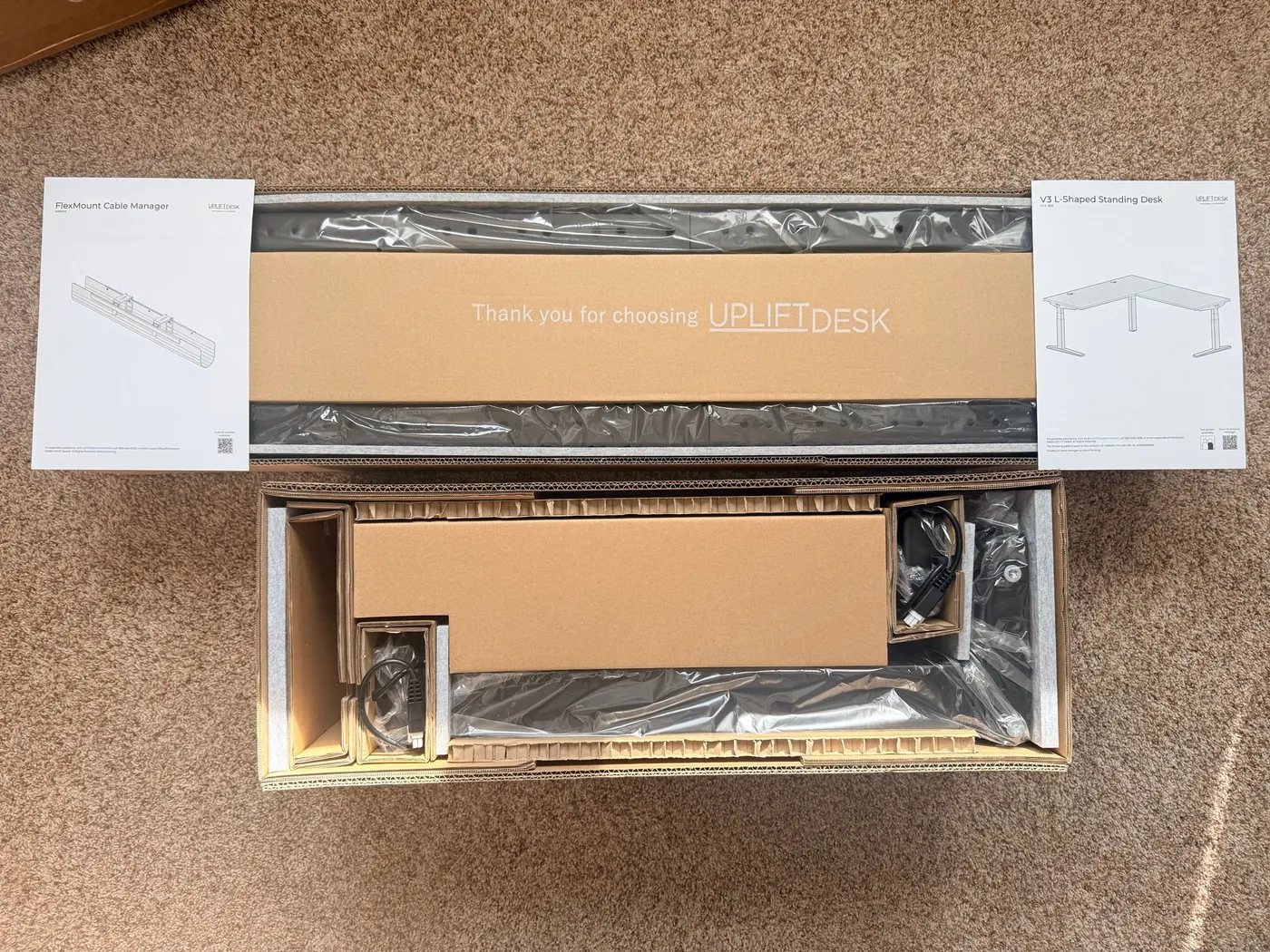 Inside the UPLIFT V3 L-Shaped frame box: foam-padded packaging with a "Thank you for choosing UPLIFTDESK" cardboard tray covering the V3 frame components