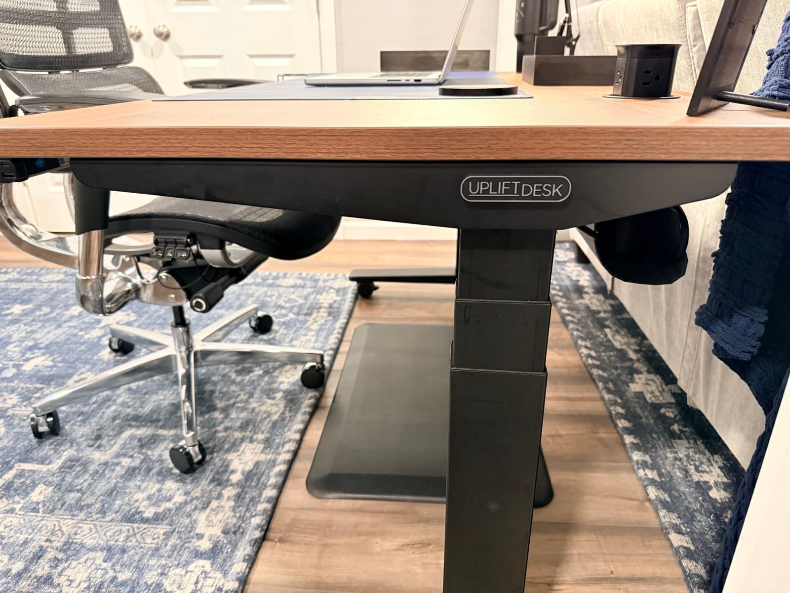 Under-desk view showing UPLIFT Desk logo, steel frame, and casters