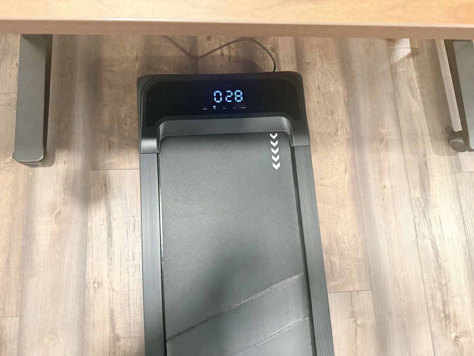 Walking pad tucked under the desk, display showing active session at 0:28